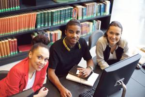 Three young people in a library sitting in front of a computer